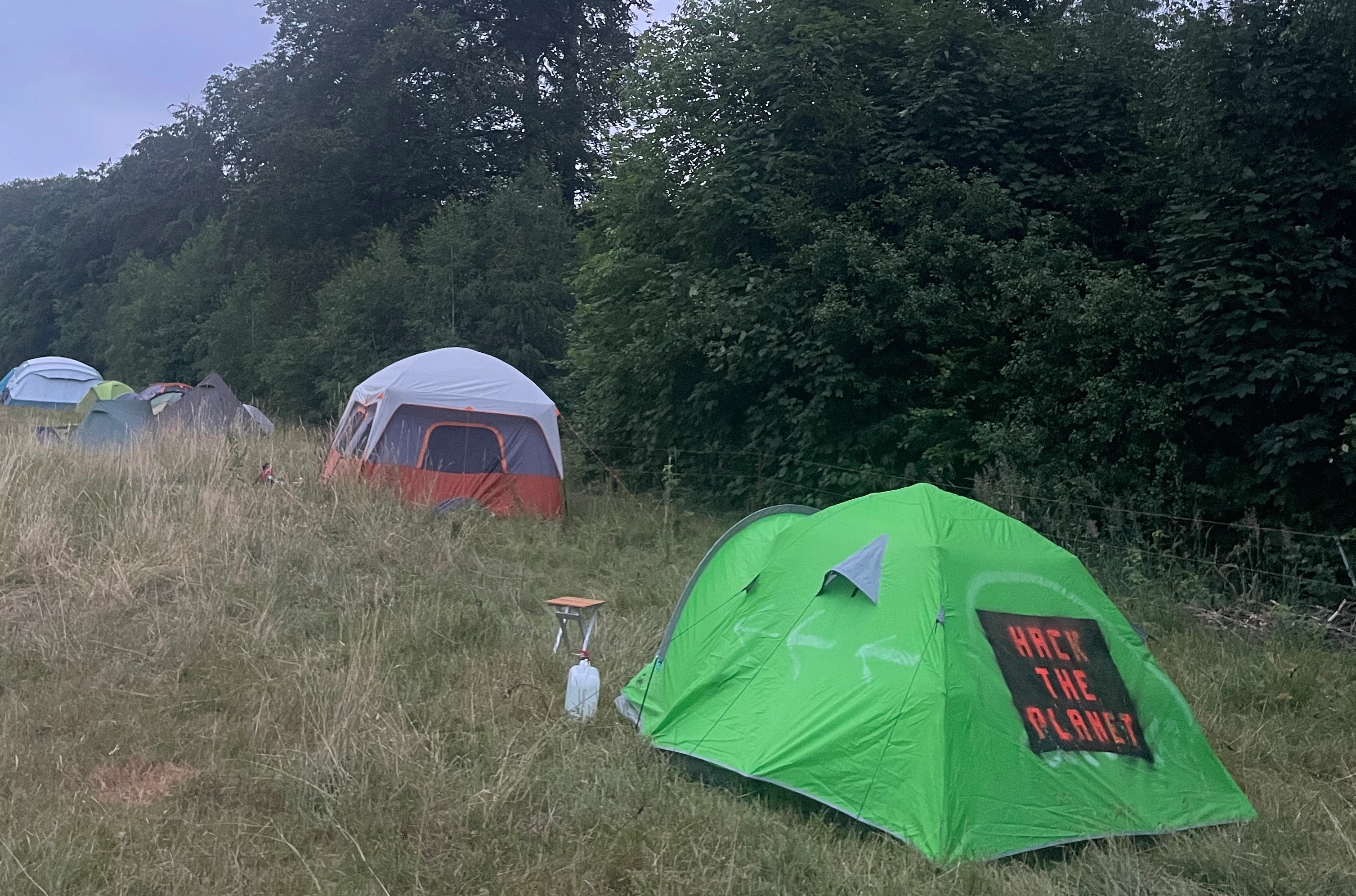 tents in a field. one has a cloth on it screenprinted with 'HACK THE PLANET'